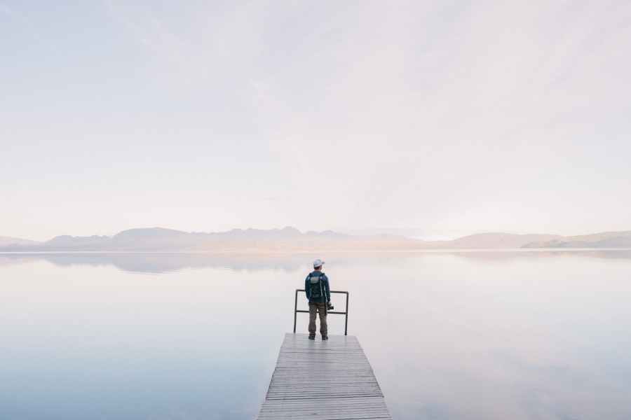 man wearing jacket standing on wooden docks leading to body of water